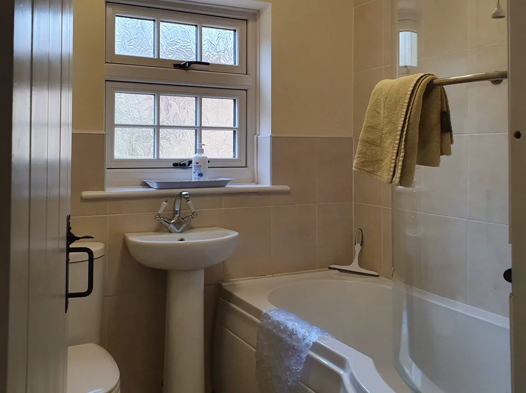 Bright bathroom with leaded glass window, pedestal sink, and tub with towel
