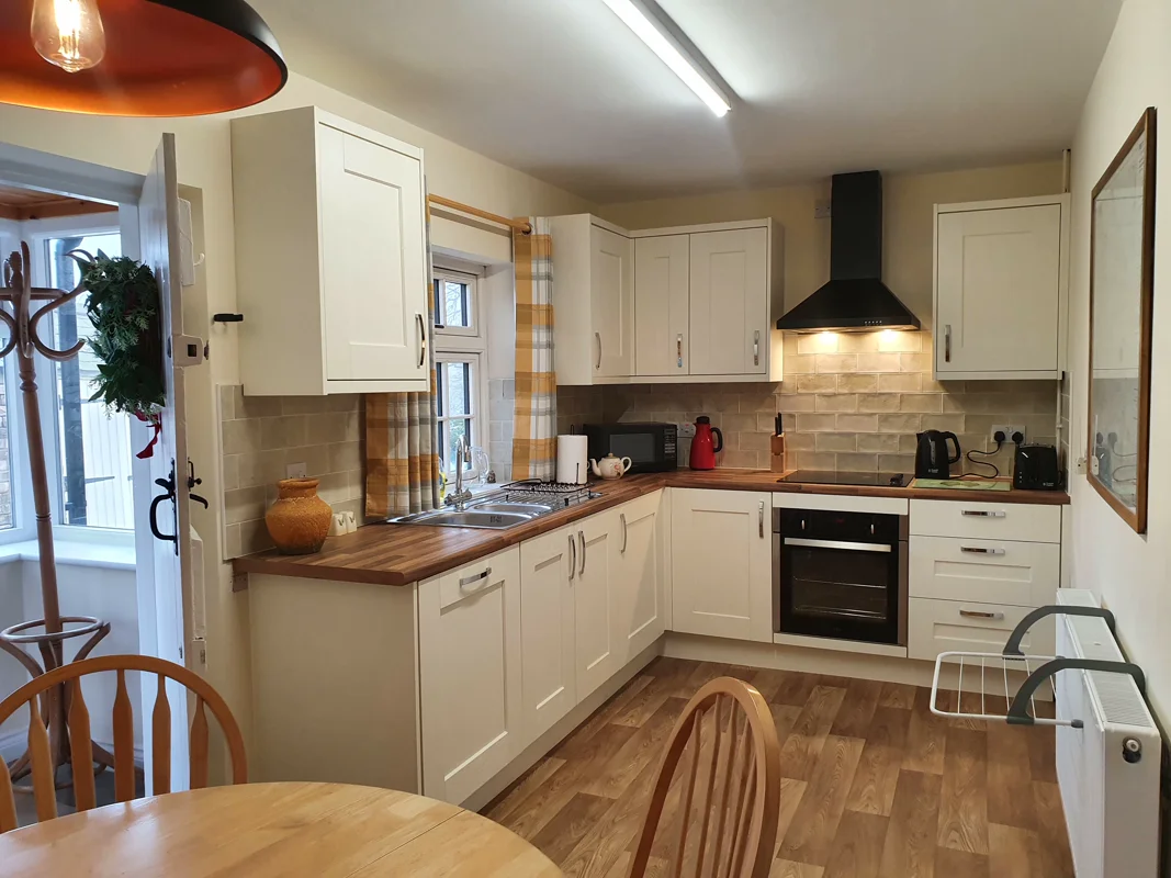 Bright kitchen with white cabinets, wooden counters, black appliances, sunlit window, and dining chairs.