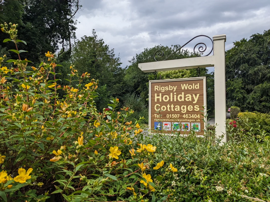 Sign for Rigsby Wold Holiday Cottages, yellow flowers and greenery.