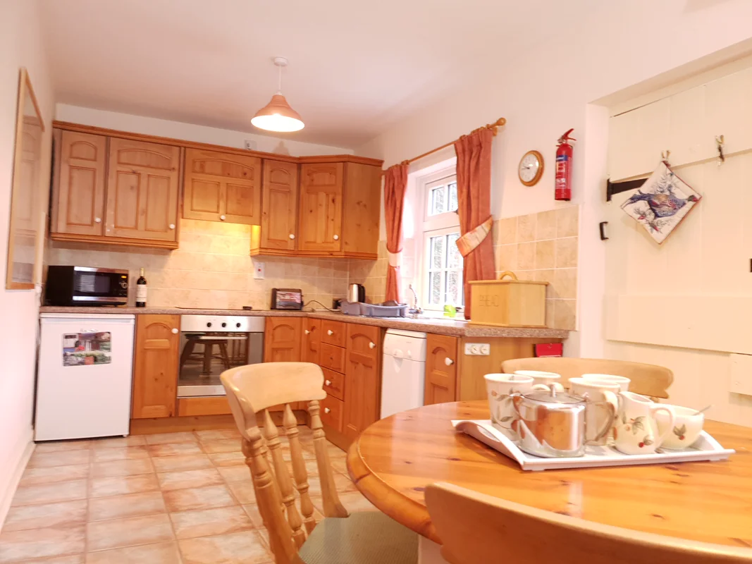 Warm wooden kitchen with round table, tea set, and window curtains in a holiday cottage.