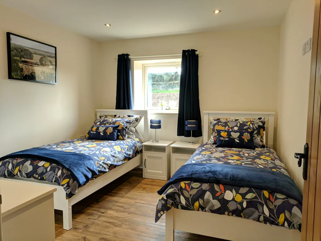 Two twin beds with floral bedding, dark blue curtains, white furniture in bright cottage bedroom