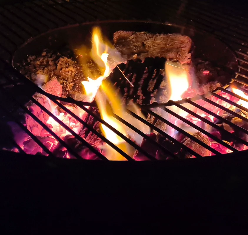 Close-up of glowing charcoal grill with flames and wood pieces on dark night