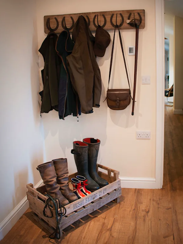 Wooden hook rack with jackets, boots in crate, leather satchel for rural home entry.